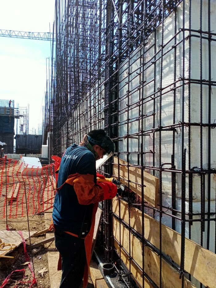 A construction worker welds metal frameworks at a busy building site, showcasing industrial safety.